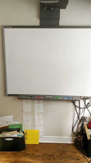 [Image of a Smart Board. Beneath it are music books and a series of pictures showing fixed do equivalents to the musical alphabet.]